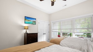 Quarto com duas camas, cômoda, televisão e janela com cortinas.