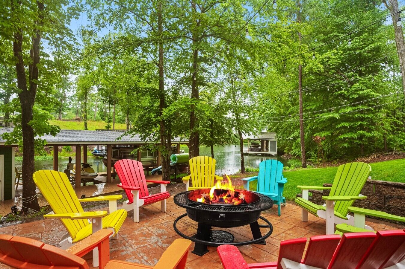 Un espace patio agrémenté de chaises Adirondack aux couleurs vives, d’un foyer extérieur et offrant une vue sur un lac.
