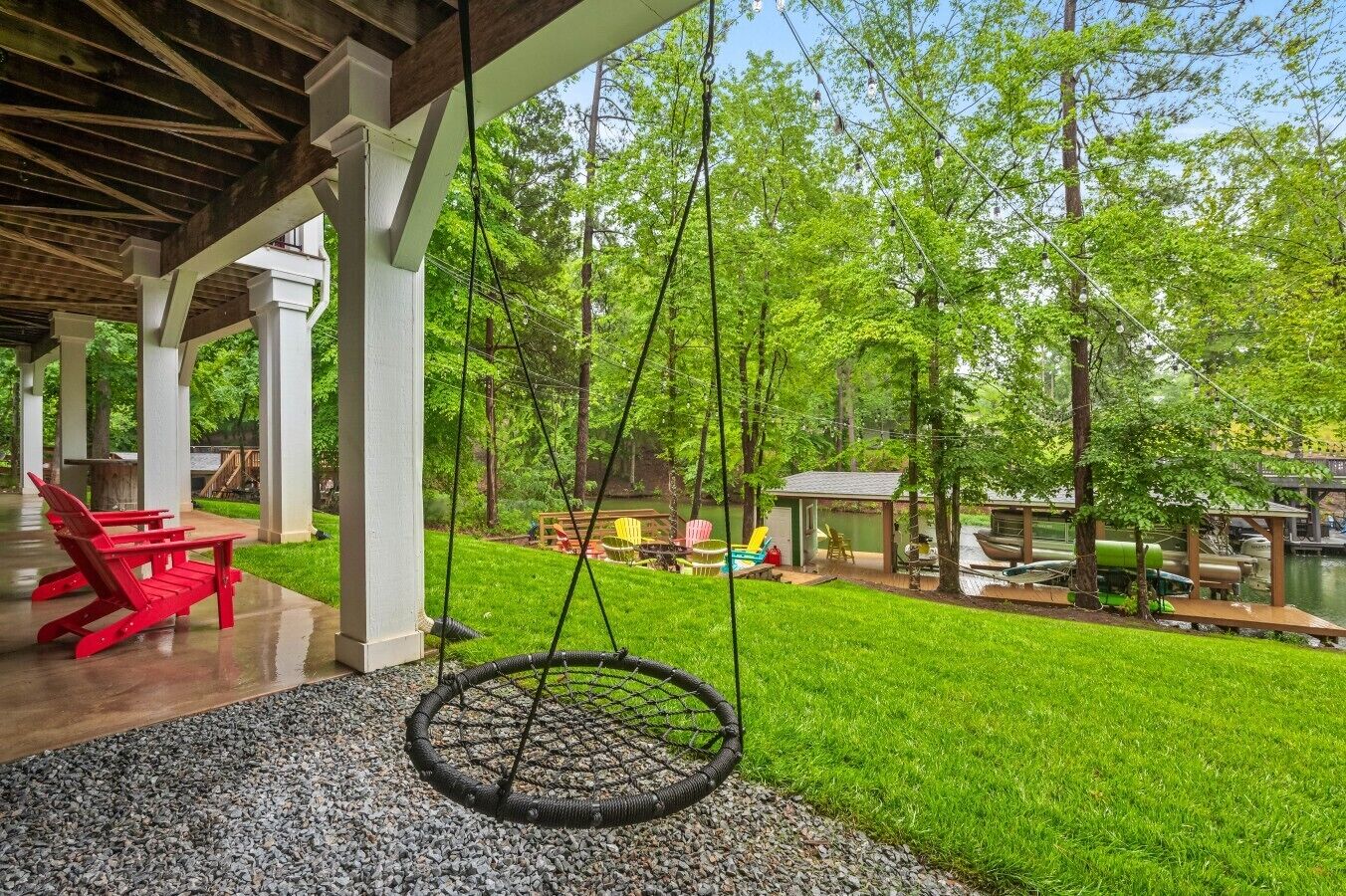 A covered patio with a swing, a red chair, and a small table.