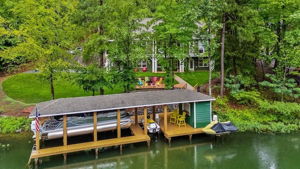 Uma casa de barcos atracada com um deck coberto, um pequeno galpão e uma área gramada com móveis de exterior.
