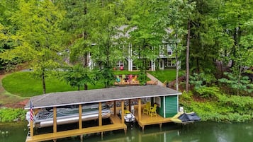 Un abri à bateaux aménagé avec une terrasse couverte, un petit cabanon et une pelouse équipée de mobilier d’extérieur.