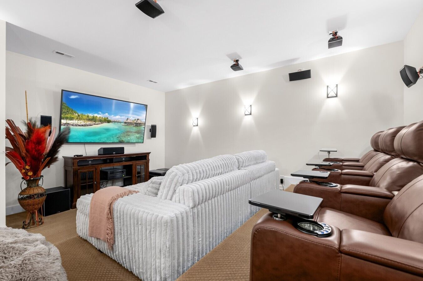 Un salon moderne doté d’un grand téléviseur à écran plat, d’un canapé blanc, d’un divan en cuir marron et d’une petite table sur laquelle se trouve un ordinateur portable.