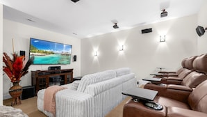 Uma sala de estar moderna com uma televisão de tela plana grande, um sofá branco, um sofá de couro marrom e uma pequena mesa com um laptop.