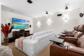 Ein modernes Wohnzimmer mit einem großen Flachbildfernseher, einem weißen Sofa, einem braunen Ledersessel und einem kleinen Tisch mit einem Laptop.
