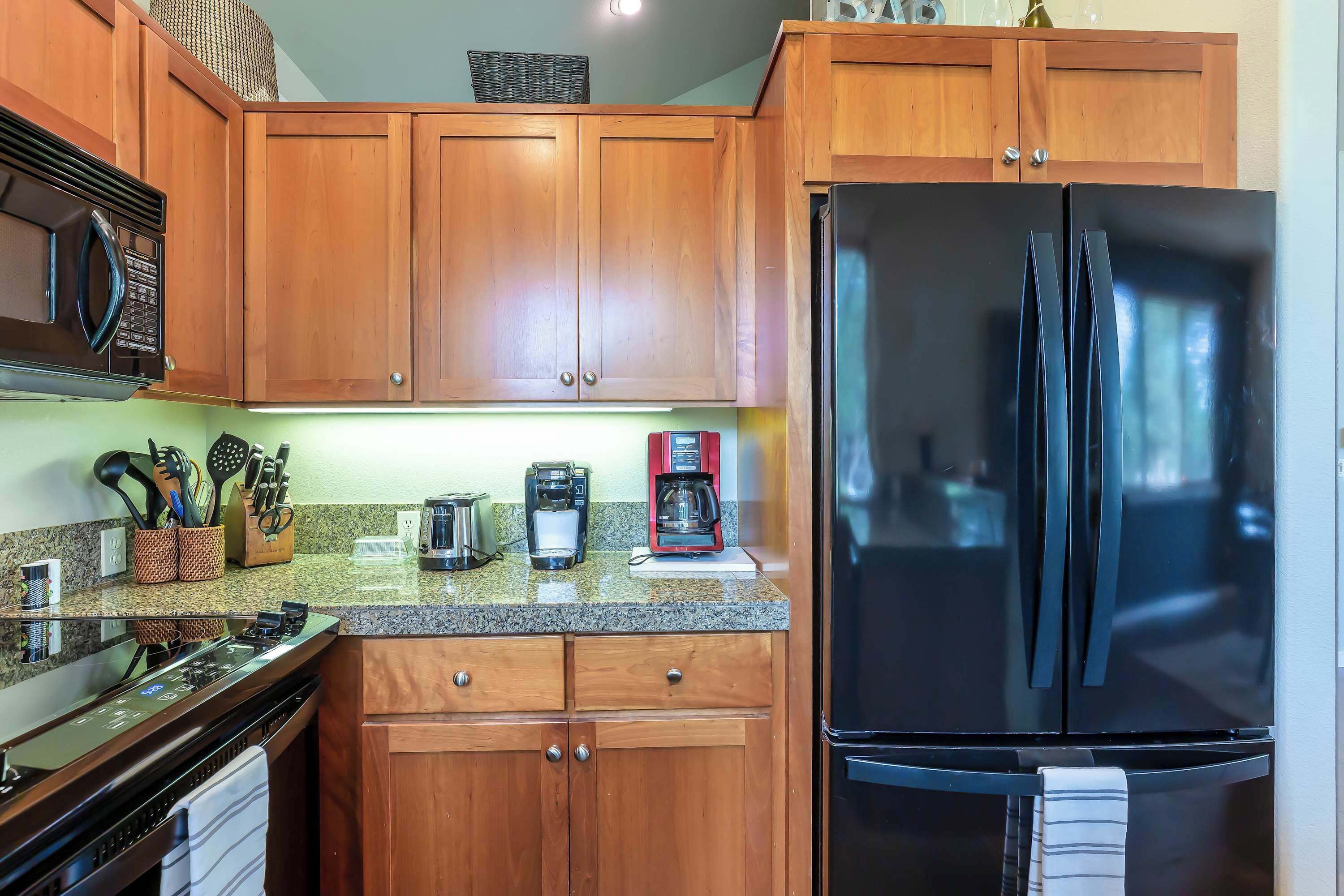 A kitchen with wooden cabinets, a black refrigerator, a microwave, a coffee maker, and a dishwasher.