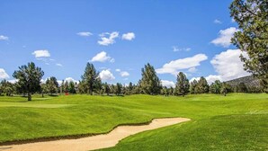 Golfkenttä, jossa on hiekkabunkkereita, puita ja kirkas taivas.