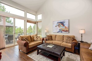 A spacious living room with a large window, a leather sofa set, a coffee table, and a painting on the wall. - Spacious Eagle Crest Condo with Resort Perks (Redmond)