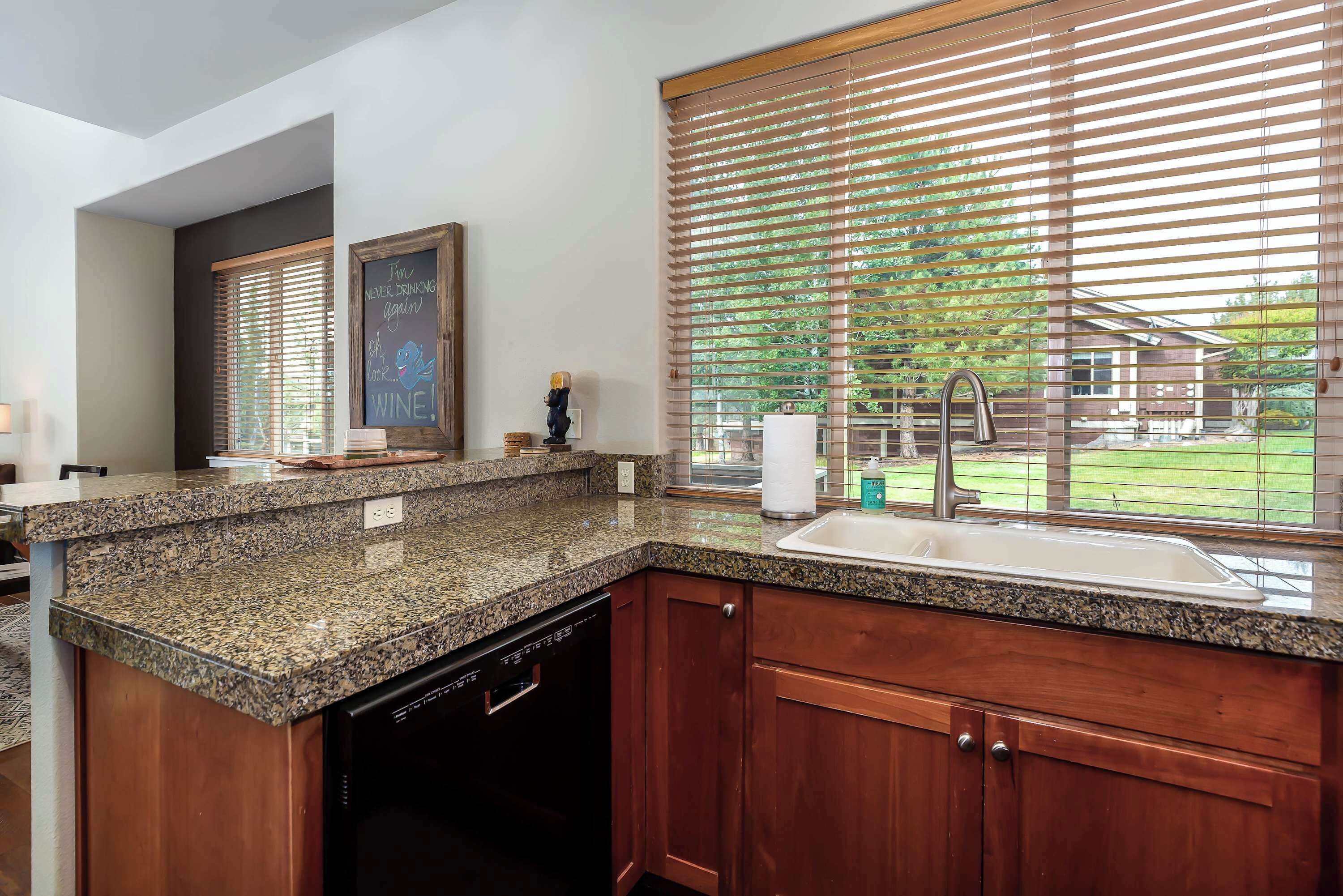 A kitchen with granite countertops, wooden cabinets, a dishwasher, a sink, and a window with blinds.