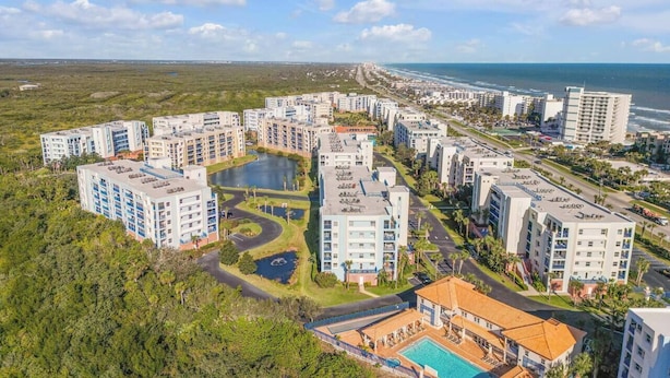 Vista aérea de una zona residencial costera con varios edificios altos, una fuente central y un área de piscina.