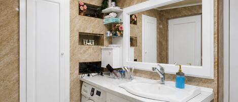 A bathroom with a washing machine, a sink, and a mirror.