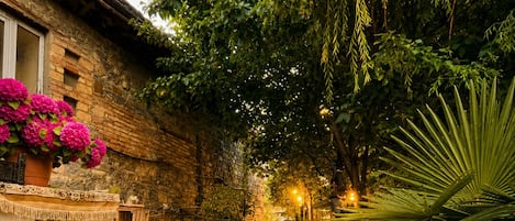 A narrow stone pathway flanked by lush greenery and a brick building with a mural.