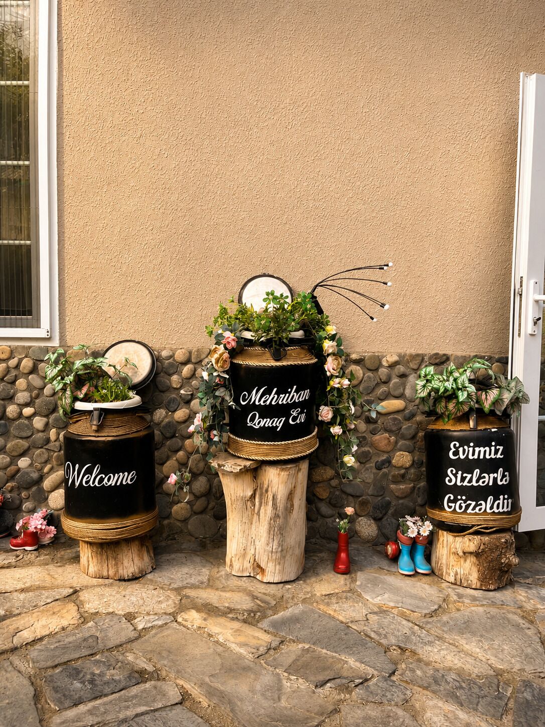 Three decorative planters with welcoming messages and potted plants against a textured wall.