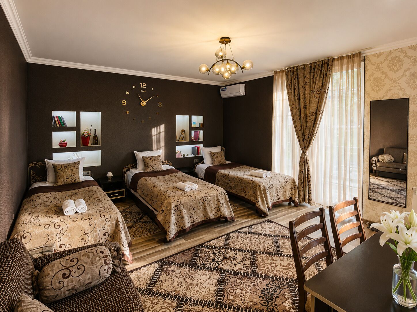 A hotel room with two beds, a dining table, a chandelier, and a large mirror.