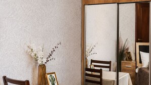 Un coin repas avec une table dressée pour deux personnes, un miroir qui reflète la pièce et un plancher en bois.