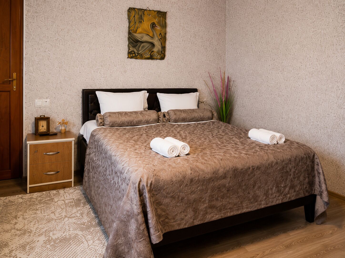 Una cama bien hecha con una colcha marrón, dos almohadas y toallas enrolladas al lado.