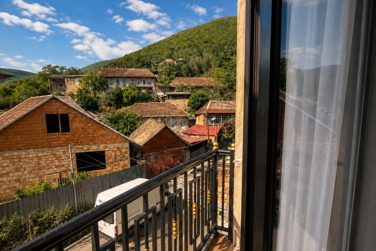 Un barrio residencial con casas, una camioneta blanca y un balcón con baranda de metal.