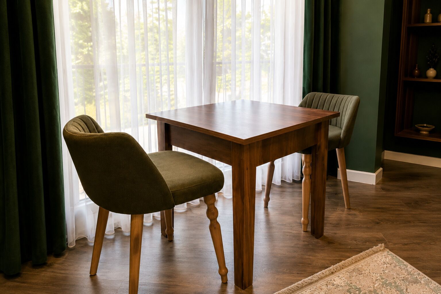 A dining area with a wooden table and two chairs, a green rug, and a bookshelf with decorative items.