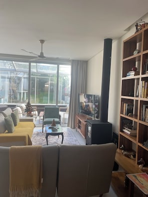 A living room with a sofa, armchairs, a coffee table, a television, a bookshelf, and a fireplace. - Charming Garden Apartment with Solarium in Ponta Delgada (Ponta Delgada)
