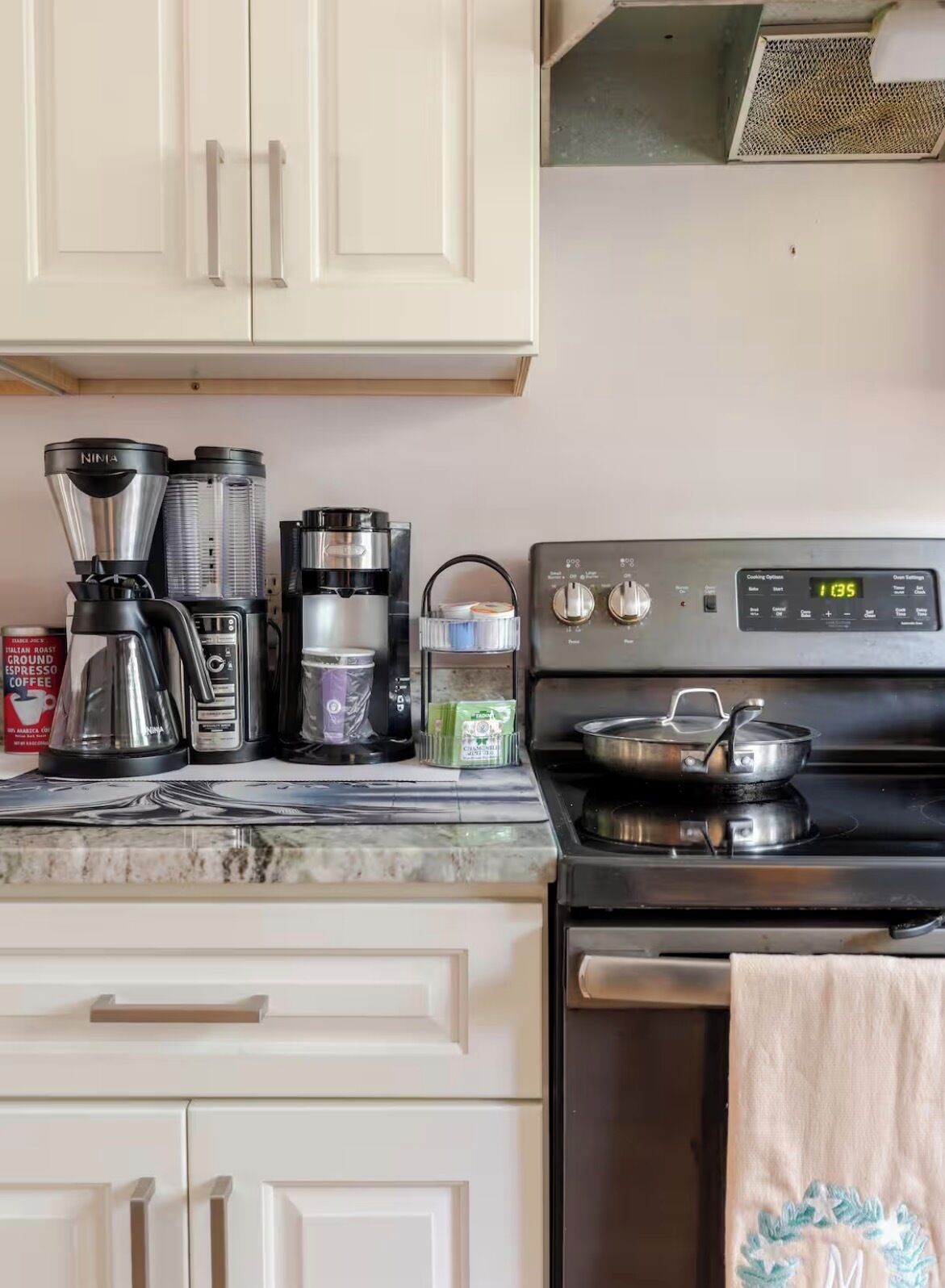 Una cocina con estufa, cafetera y hervidor.