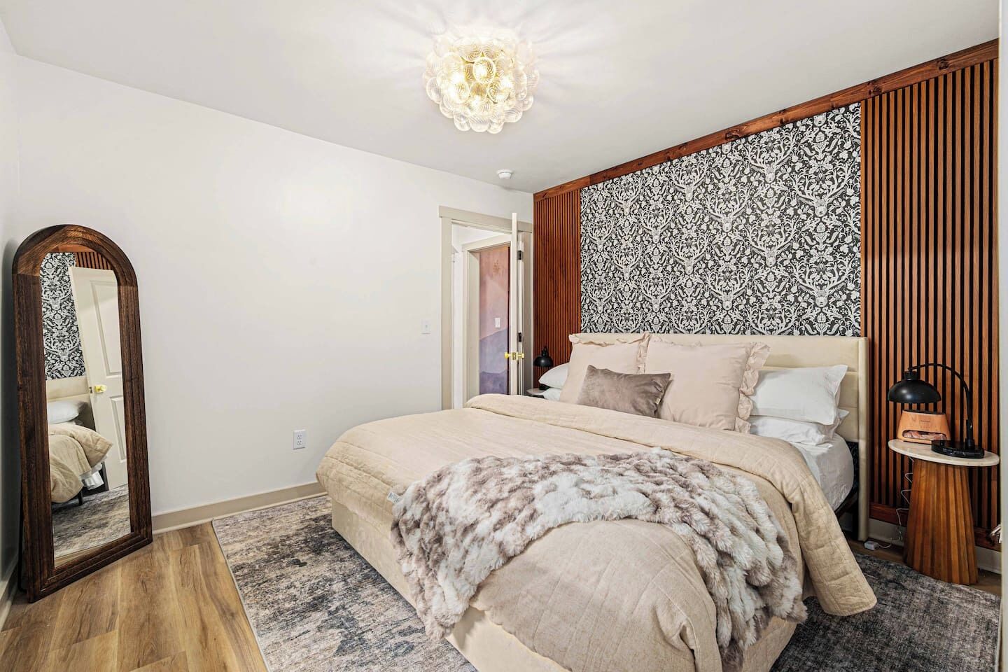 Une chambre à coucher avec un lit, un miroir, une tête de lit à motifs, une table de chevet avec une lampe et un plancher en bois.