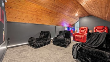 A room with a sloped ceiling, two black cushioned chairs, a red leather chair, and a small table with a neon sign in the background.