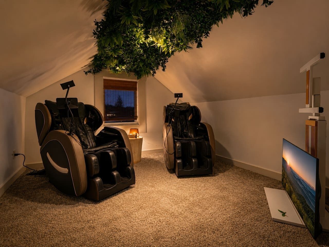 Ein Zimmer mit zwei Massagesesseln, einem kleinen Tisch mit Lampe und einem Bild an der Wand.