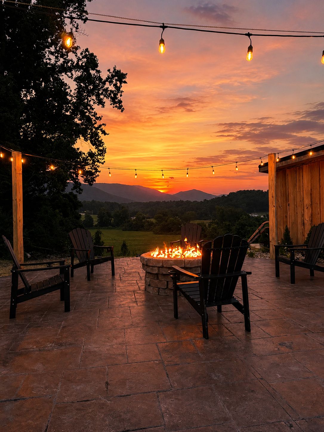 An outdoor seating area with chairs and a fire pit, under string lights, with a sunset view.