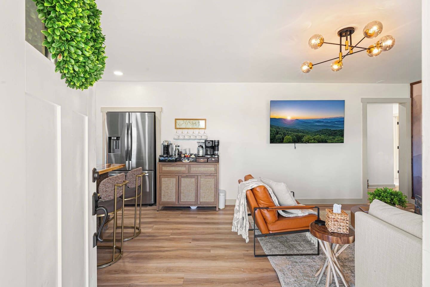Eine moderne Küche mit Edelstahl-Kühlschrank, einer Essecke mit Barhocker, einer Couch und einem großen Landschaftsbild an der Wand.