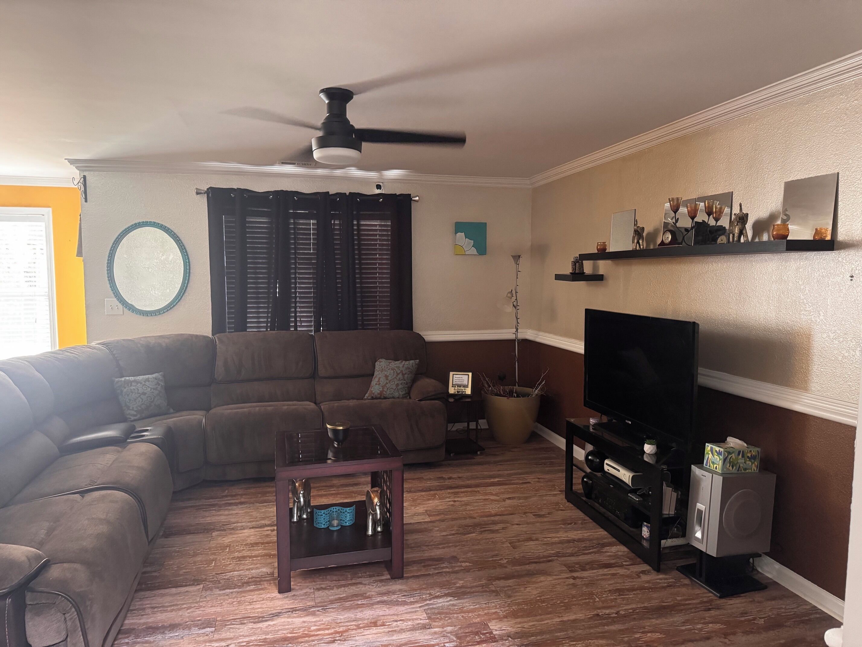 A living room with a sectional sofa, a coffee table, a TV, and a ceiling fan.