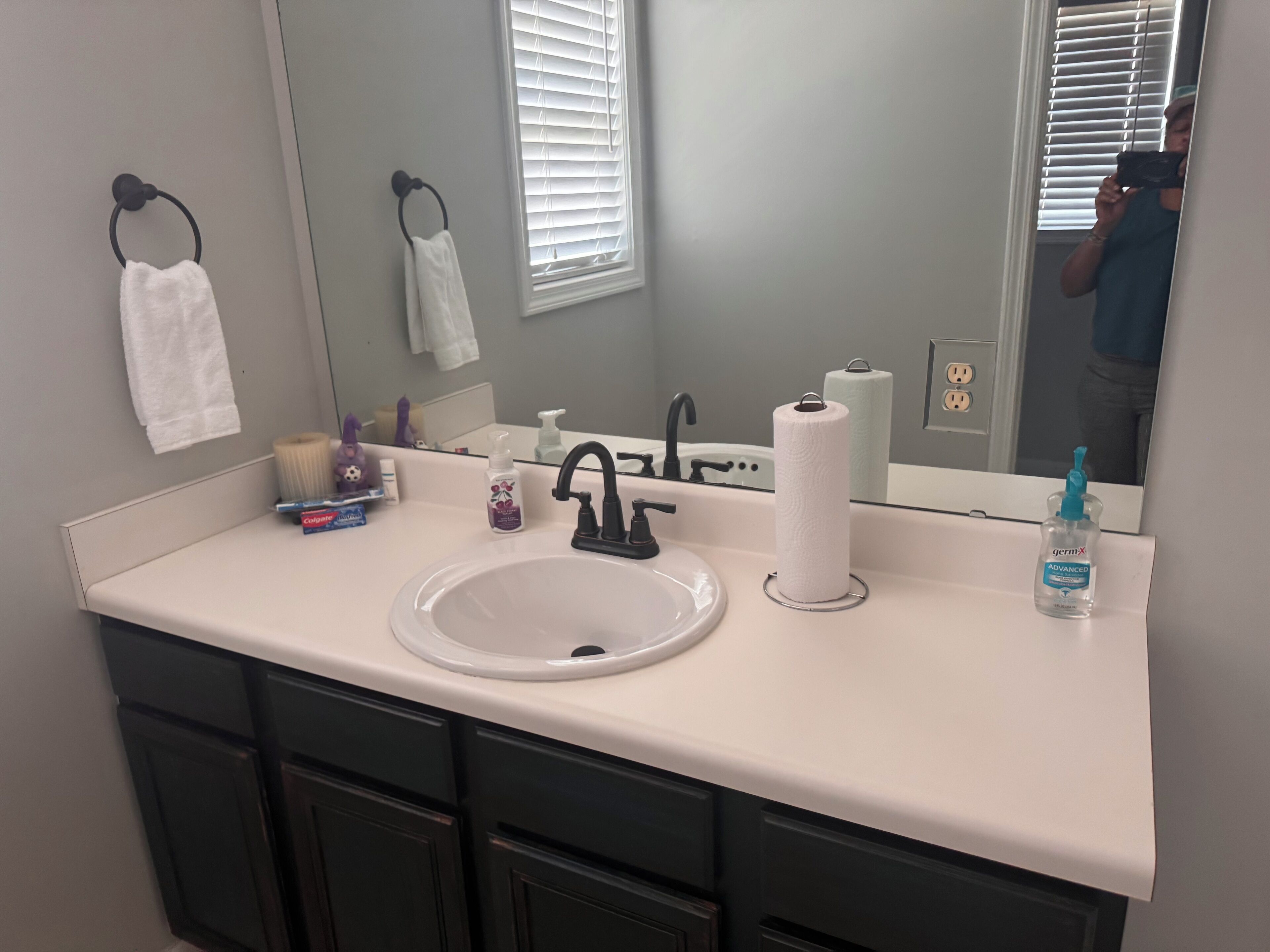 A bathroom with a white sink, black faucet, and a mirror reflecting a person taking a photo.