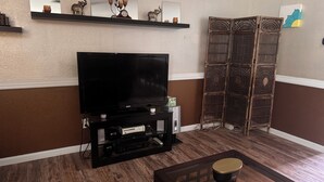 A living room with a flat-screen TV, wooden entertainment unit, decorative wall shelves, and a traditional woven partition.