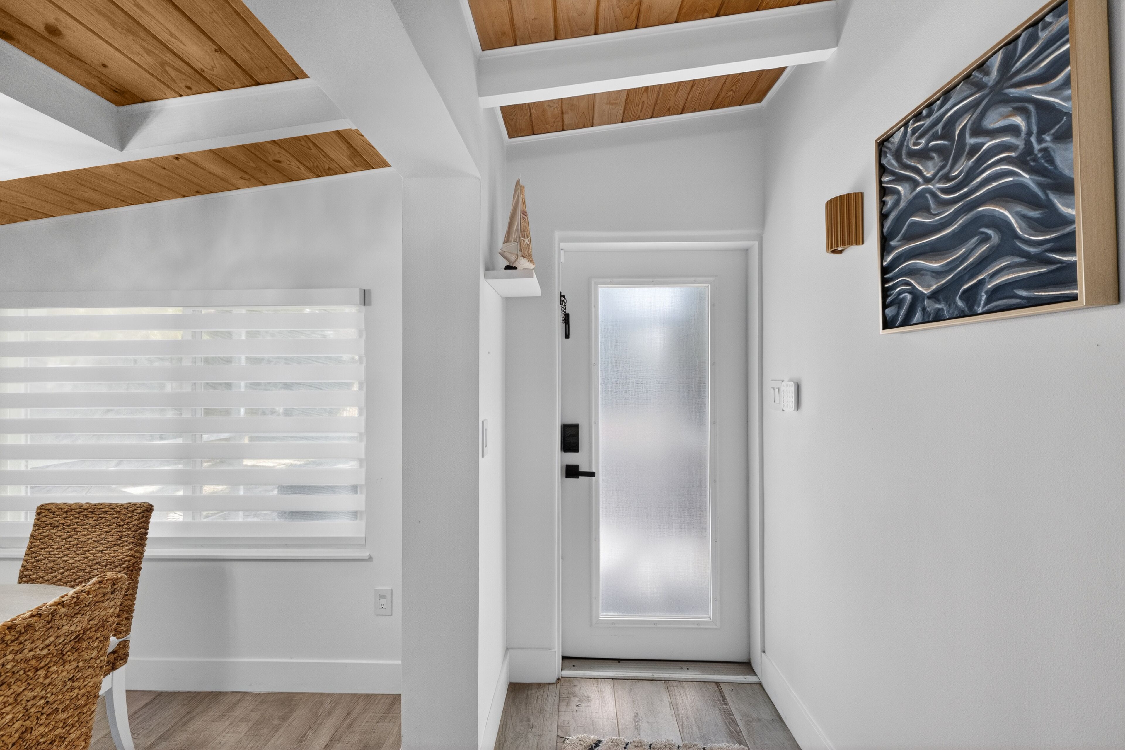 A hallway with a white door, a wall-mounted light fixture, and a woven chair.