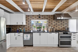 Eine moderne Küche mit weißen Schränken, einem Edelstahlkühlschrank, einem Gasherd und einer strukturierten Spritzschutzwand.