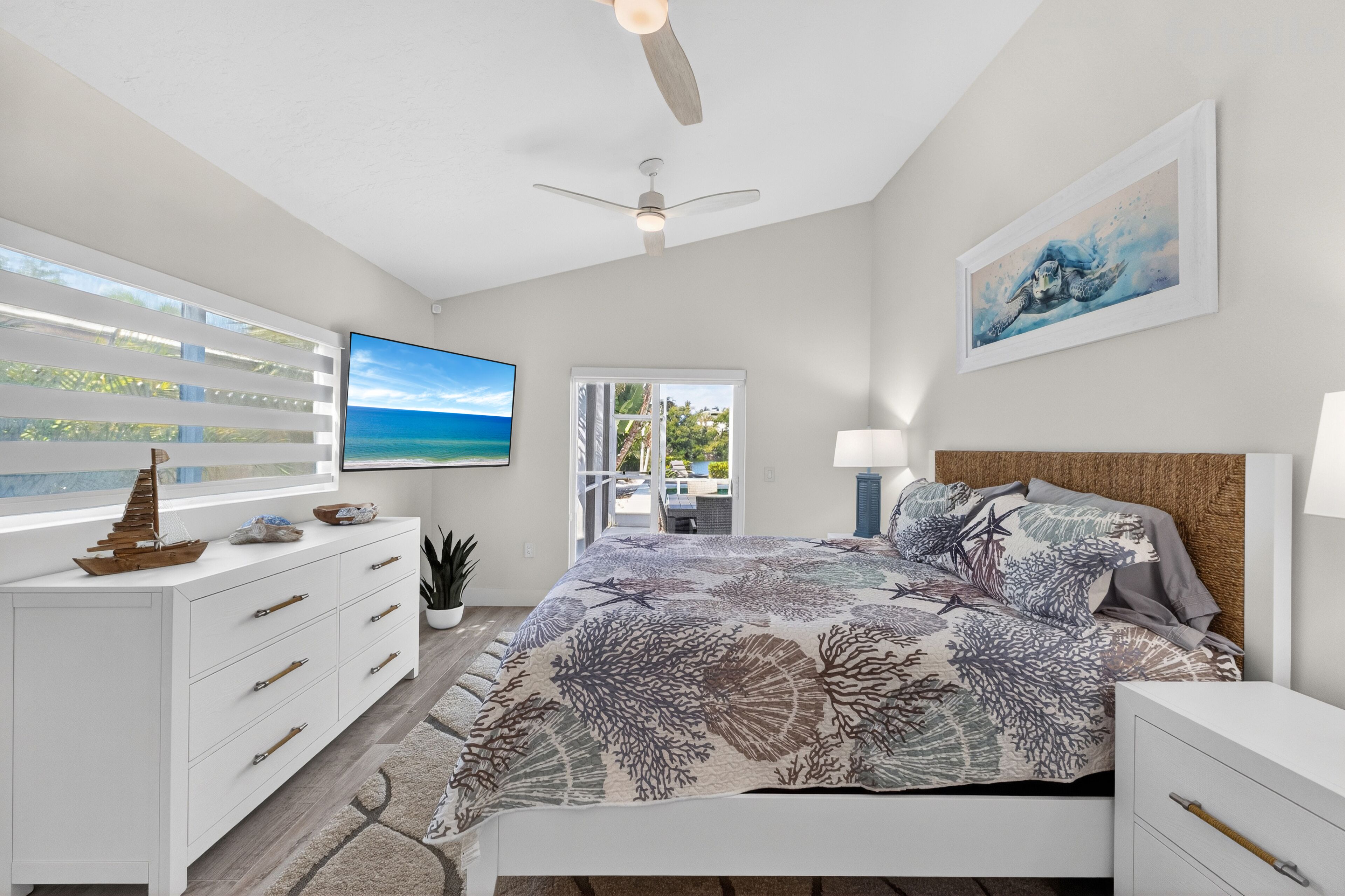 A bedroom with a bed, a dresser, a ceiling fan, a TV, and a painting.