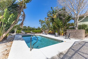 A rectangular swimming pool with a metal ladder, surrounded by palm trees and other tropical plants.