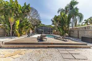 A backyard with a pool, lounge chairs, and a wooden deck. - Waterfront Home with Pool and Hot Tub  (Sarasota)