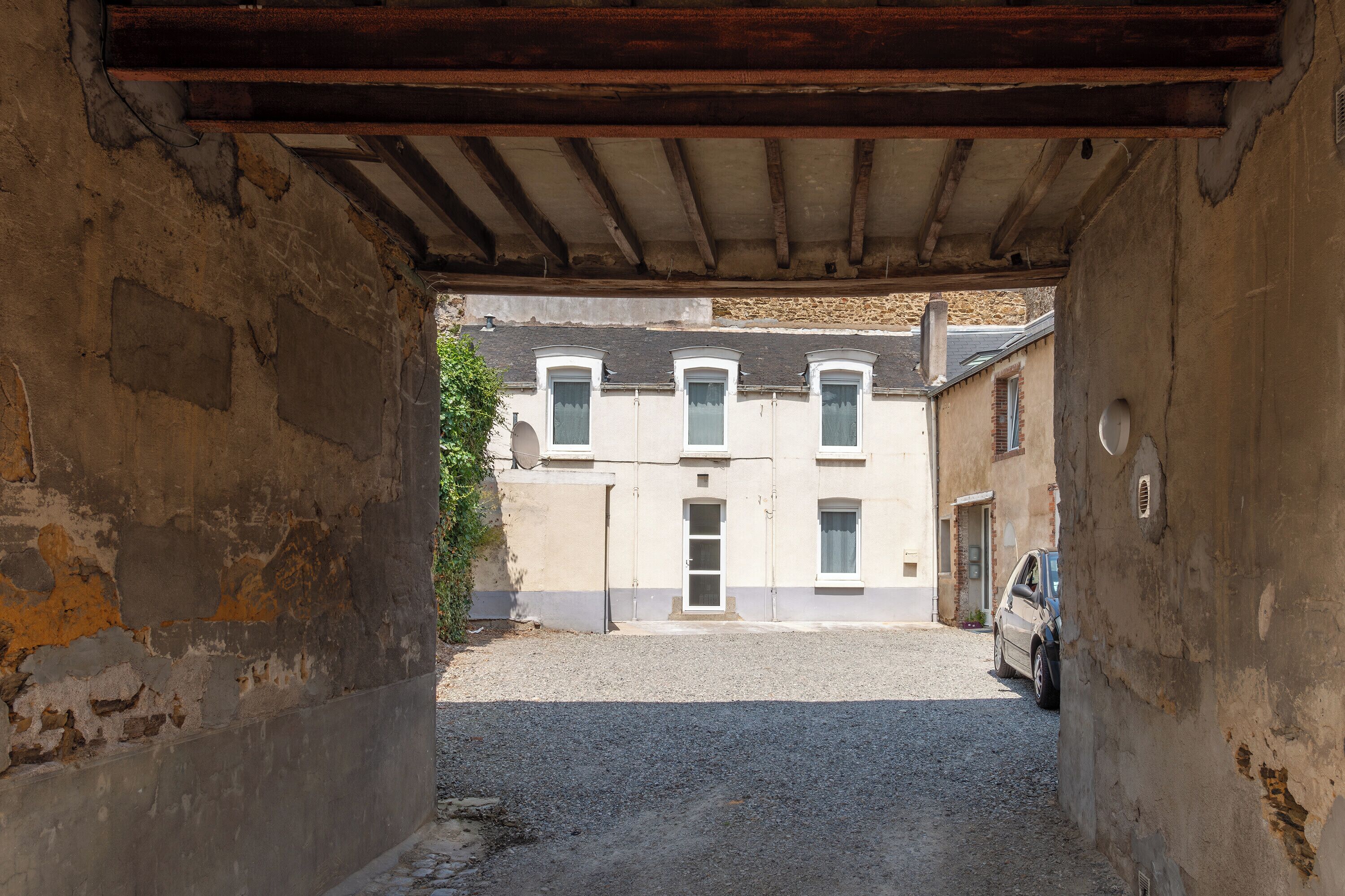 A narrow alleyway leading to a building with a row of windows and a car parked outside.