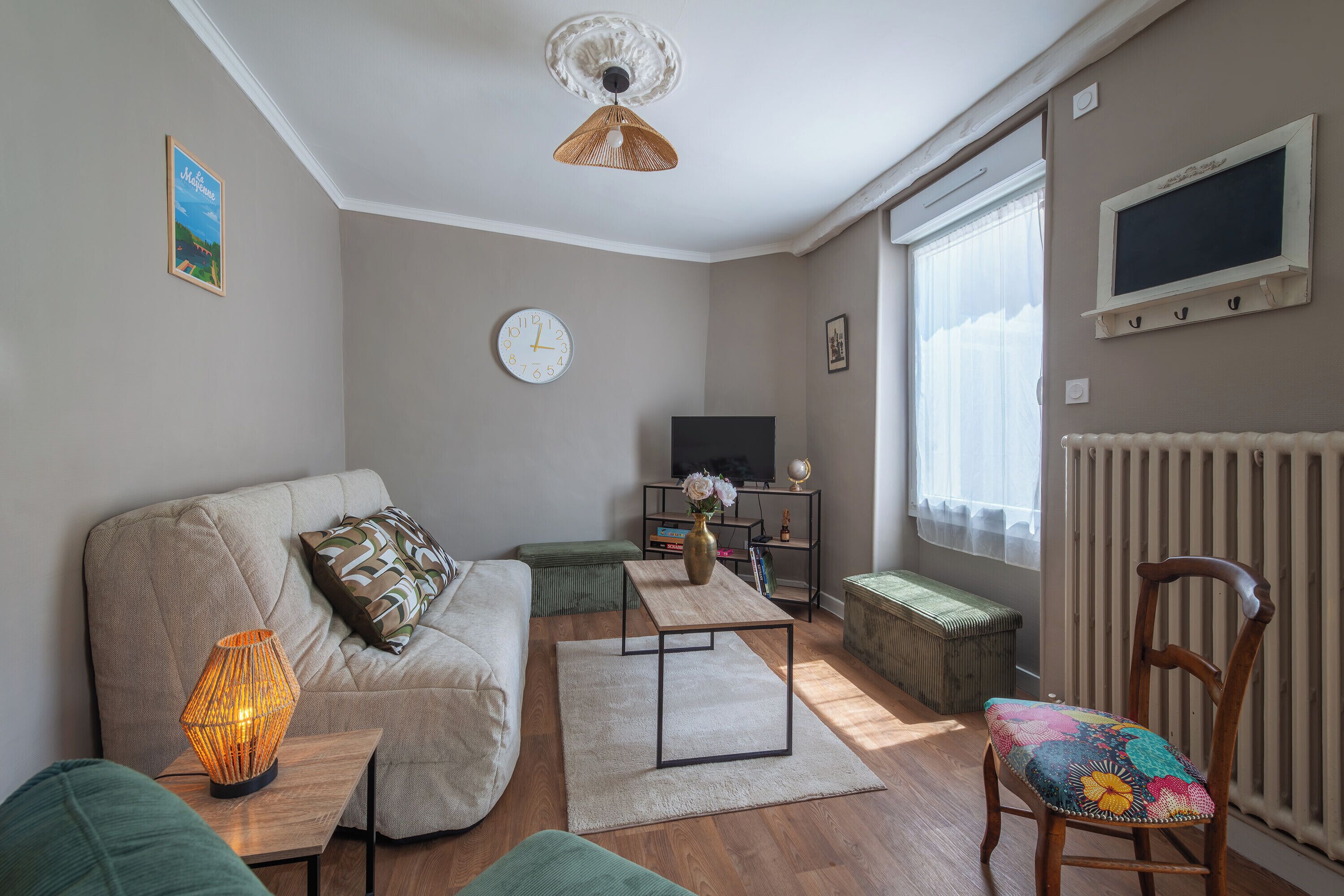 A living room with a sofa, a coffee table, a chair, a TV, and a radiator.