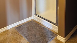 A corner of a room with a glass door, a doormat, and a wall with a textured finish. - Modern Duplex with 3 bedroom (Dawson Creek)
