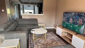 A modern living room with a sectional sofa, a small round table, a TV on a wooden stand, and a patterned rug. - Modern Duplex with 3 bedroom (Dawson Creek)