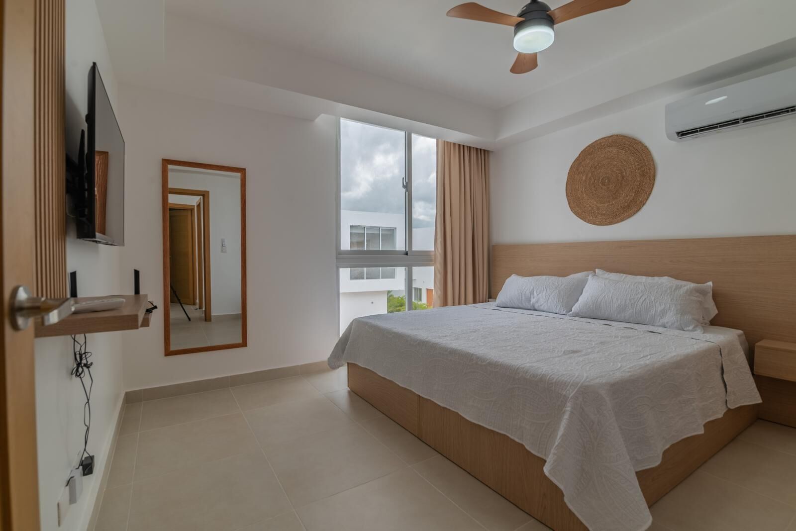 A bedroom with a bed, a ceiling fan, a TV, and a window with curtains.