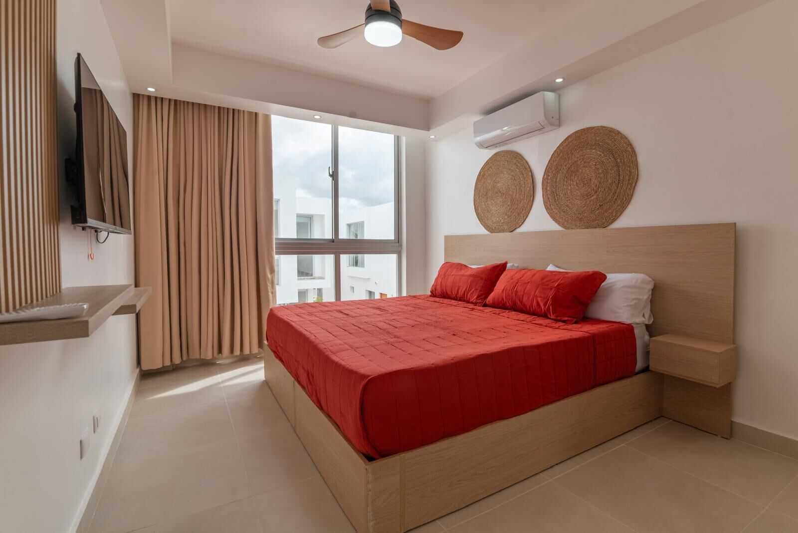 Una camera da letto moderna con un letto, una TV, un ventilatore a soffitto e una grande finestra.