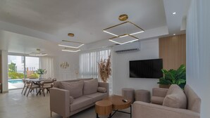 Ein modernes Wohnzimmer mit Sofa, Couchtisch und Fernseher. Es gibt einen Essbereich mit Tisch und Stühlen.