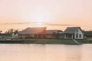 A house with a thatched roof and a modern building, situated by a calm body of water. - Bright 3BR Villa with Private Pool in Punta Cana By Vistacana (Punta Cana)