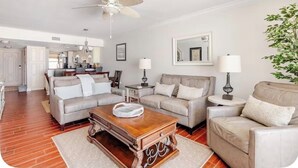 A living room with a wooden coffee table, two sofas, a ceiling fan, and a kitchen in the background. - Little Bit of Paradise, Direct Beachfront, Stunning Sunsets, Sleeps 6 (Clearwater)
