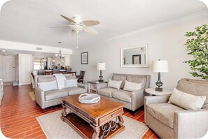 A living room with a wooden coffee table, two sofas, a ceiling fan, and a kitchen in the background. - Little Bit of Paradise, Direct Beachfront, Stunning Sunsets, Sleeps 6 (Clearwater)