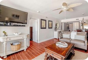 A living room with a television, a ceiling fan, a sofa, and a coffee table. - Little Bit of Paradise, Direct Beachfront, Stunning Sunsets, Sleeps 6 (Clearwater)