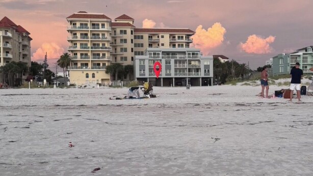A beach with buildings in the background, a red location marker, and a few people. - Little Bit of Paradise, Direct Beachfront, Stunning Sunsets, Sleeps 6 (Clearwater)