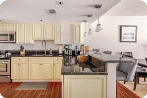 A modern kitchen with cream-colored cabinets, a granite countertop, and stainless steel appliances. - Little Bit of Paradise, Direct Beachfront, Stunning Sunsets, Sleeps 6 (Clearwater)