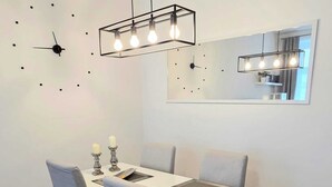 A dining area with a white table, grey chairs, a modern pendant light, a wall clock, and a mirror. - Schönbrunn Apartment - Spacious and Tastefully Decorated, Close to the City Center (Wien)